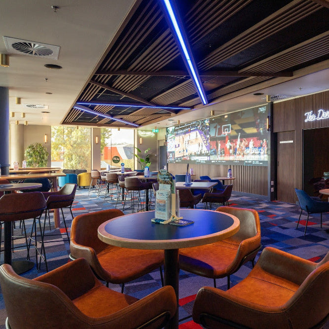 Modern bar interior with tables, chairs, and a large screen TV.