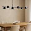 Modern black pendant light over a wooden dining table with beige chairs in a room with beige walls and a curtain.