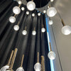 Modern chandelier with glass globe lights and gold accents against a dark curtain background.