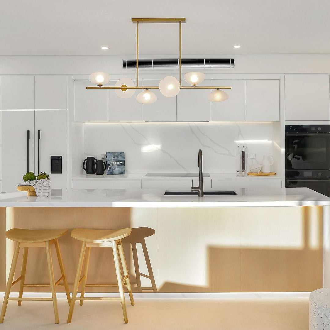 Modern kitchen with white island, bar stools, and sleek appliances. Luxury brushed brass linear chandelier